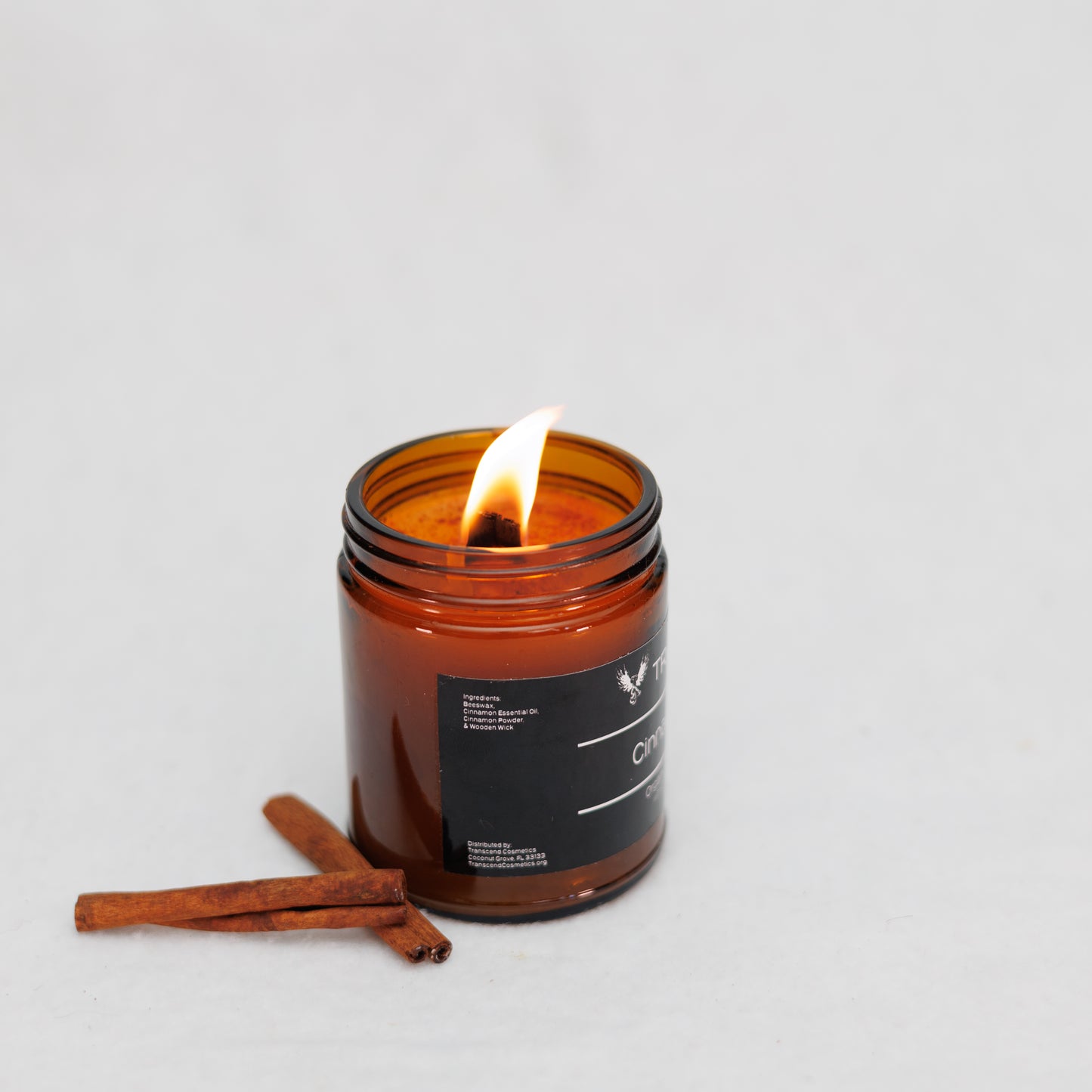 Image showing the ingredient list on the Transcend Cosmetics Cinnamon Cabin Organic Beeswax Candle, in an amber glass jar with a wooden wick, burning with a warm flame, surrounded by dried Cinnamon sticks, highlighting its natural and soothing ingredients.
Ingredients are: Beeswax, Cinnamon Essential Oil, Cinnamon Sticks, & Wooden Wick. 